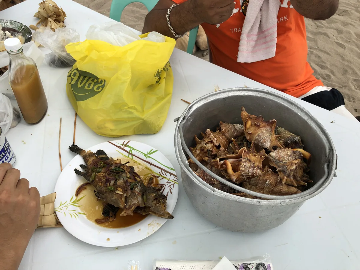テーブルに置かれた煮つけの魚と、茹でた巻貝が入った鍋