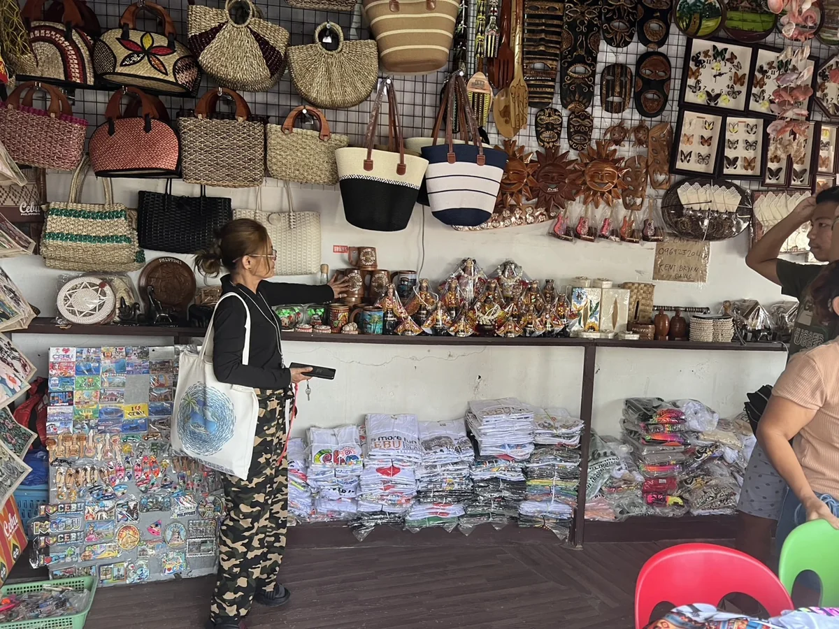 セブ島のローカルお土産屋の店内。壁一面にカゴバッグ、木彫りの仮面、蝶の標本、マグネットが並ぶ