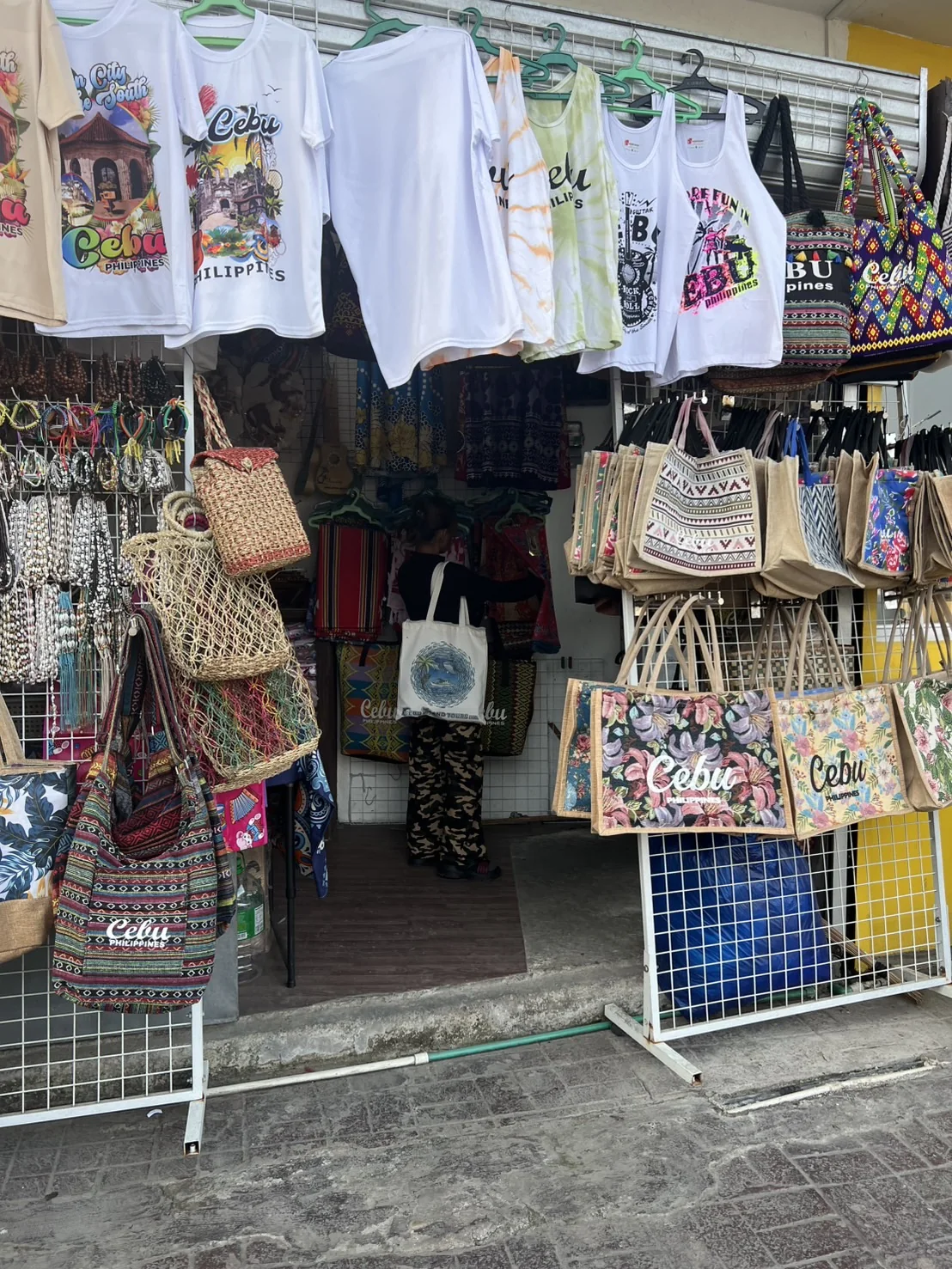 セブ島コロン周辺のローカルお土産屋の店先。TシャツとCebuのロゴ入りカゴバッグが並ぶ