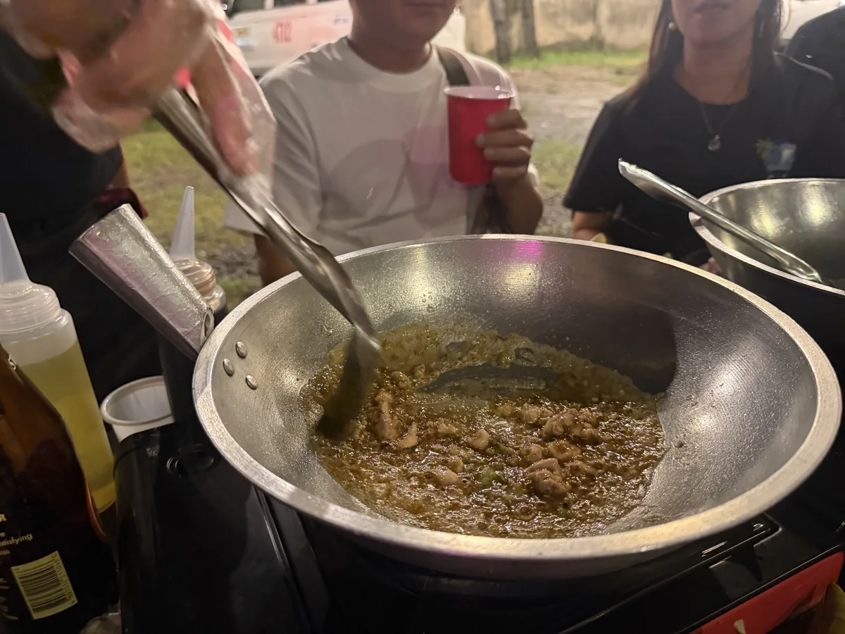 煮詰まって茶色く泡立った完成状態のトゥスロブワを鉄鍋の中でトングで混ぜている