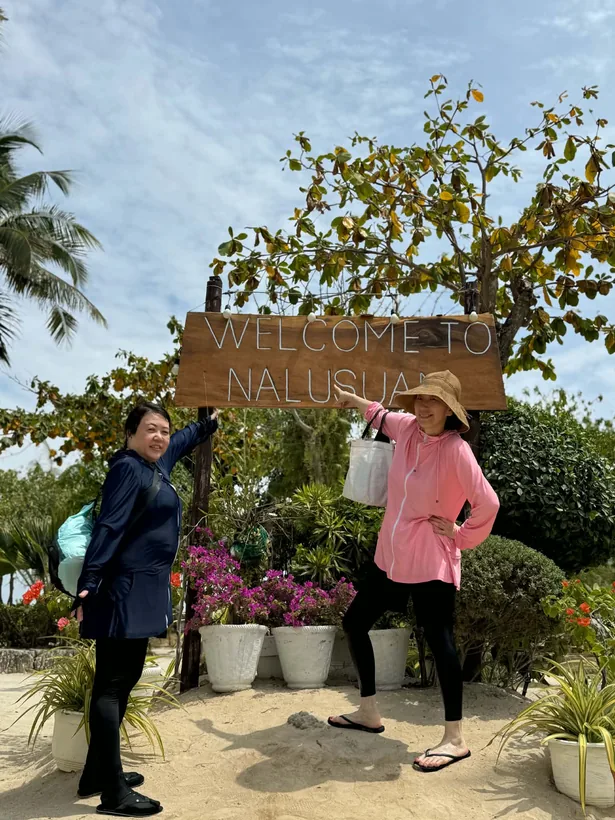ナルスアン島の WELCOME TO NALUSUAN の木の看板を指さす女性2名様
