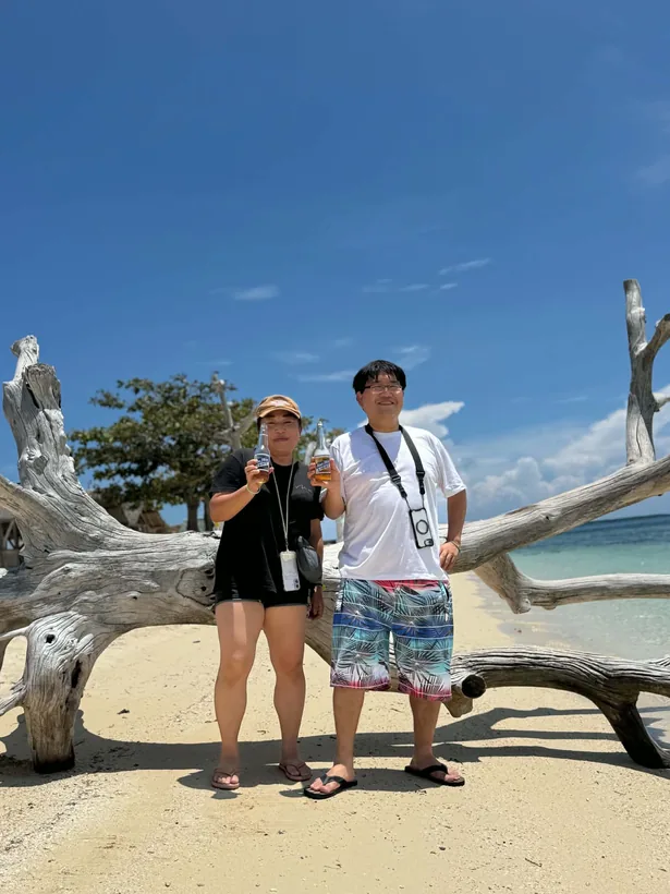 パンダノン島の白い流木の前でビールを手に記念撮影する2名様