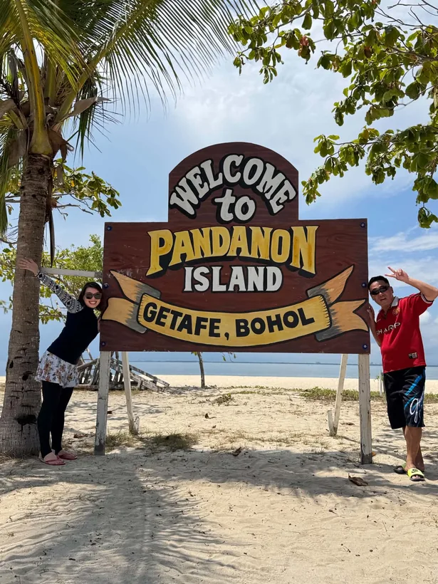 パンダノン島の WELCOME to PANDANON ISLAND の看板の前でポーズをとる2名様