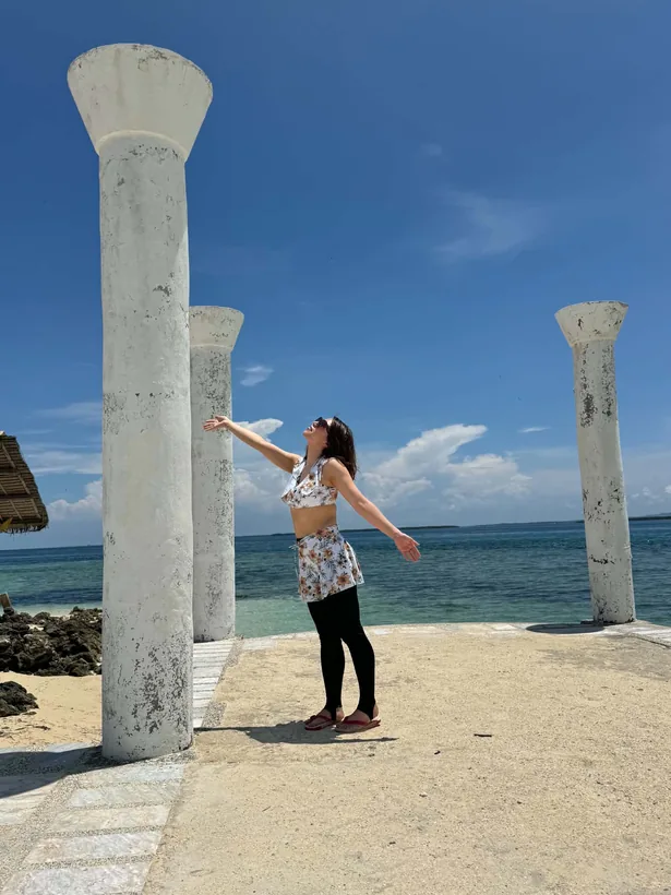 パンダノン島の海辺に立つ白い柱の間で両手を広げる女性 セブ島アイランドホッピング