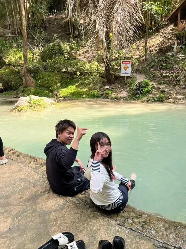 ツマログ滝の水辺に足をつけてドクターフィッシュを体験するおふたり
